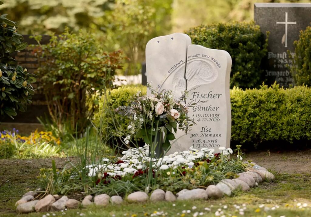 Ein schöner moderner Grabstein aus hellem Kalkstein, harmonisch gestaltet mit einer Frühjahrsbepflanzung. Die Grabstätte ist mit einer Umrandung aus Steinen liebevoll gestaltet.