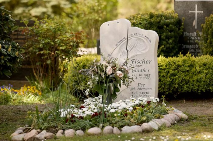 Ein schöner moderner Grabstein aus hellem Kalkstein  harmonisch gestaltet mit einer Frühjahrsbepflanzung. Die Grabstätte ist mit einer Umrandung aus Steinen liebevoll gestaltet.