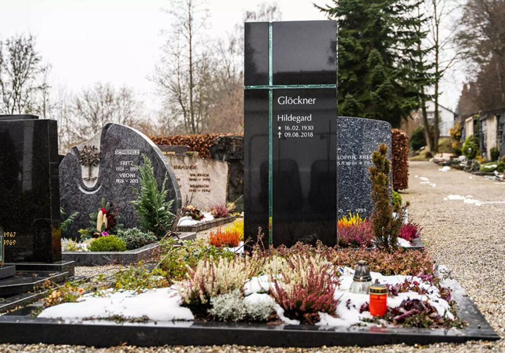 Modernes Einzelgrab mit schwarzem Granitgrabstein und christlichem Kreuz-Symbol aus Glas - winterliche Grabbepflanzung mit Bodendeckern und kleinen Stauden
