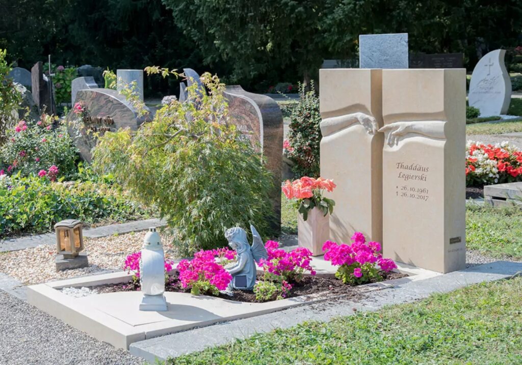 Ein geteiltes Grabmal mit berührenden Händen aus beigem Marmor, umgeben von einer Grabeinfassung und einem Bepflanzungsstreifen als Beispiel für eine Sommergrabgestaltung.