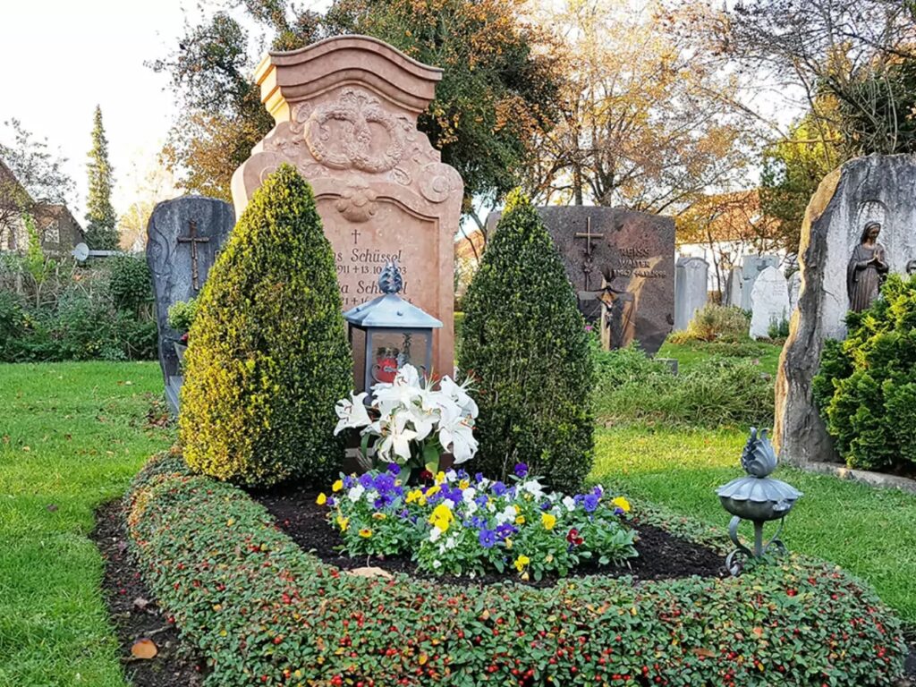 Große Grabstätte mit immergrüner Grabbepflanzung und Grabbegrenzung aus einer niedrigen Hecke.