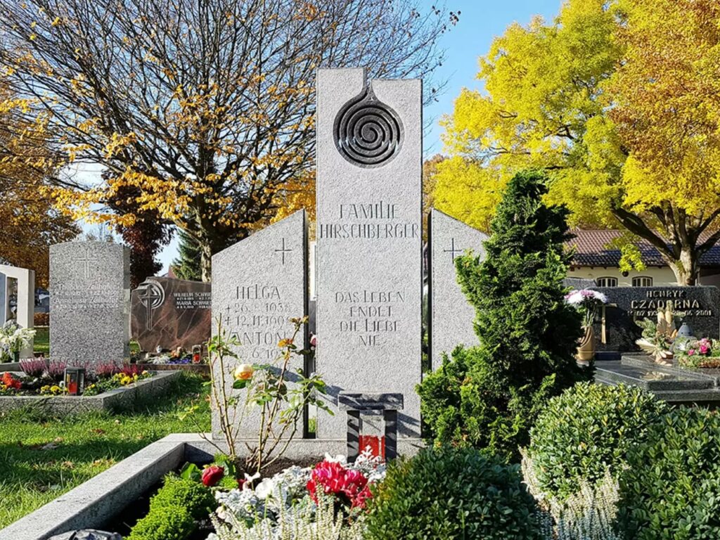 Ein moderner Grabstein für ein Doppelgrab, mehrteilig aus Granit gestaltet, verziert mit dem Symbol der Spirale, ergänzt durch eine schöne Grabbepflanzung.