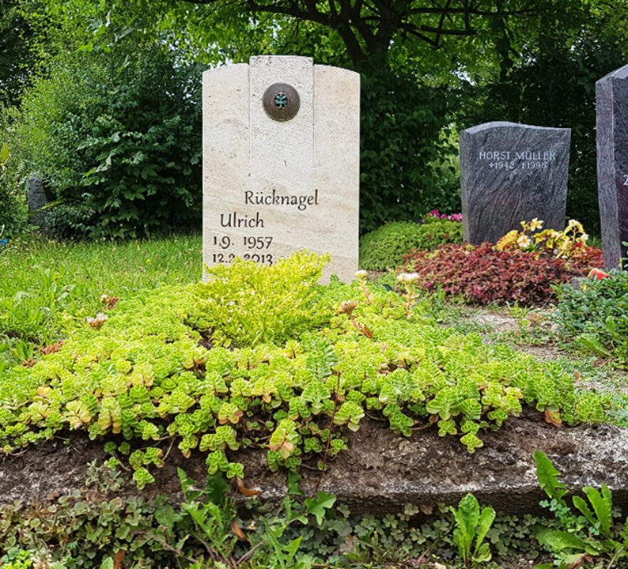 Grabstein aus Travertin mit Bronze Element für ein Einzelgrab mit immergrüner Grabbepflanzung