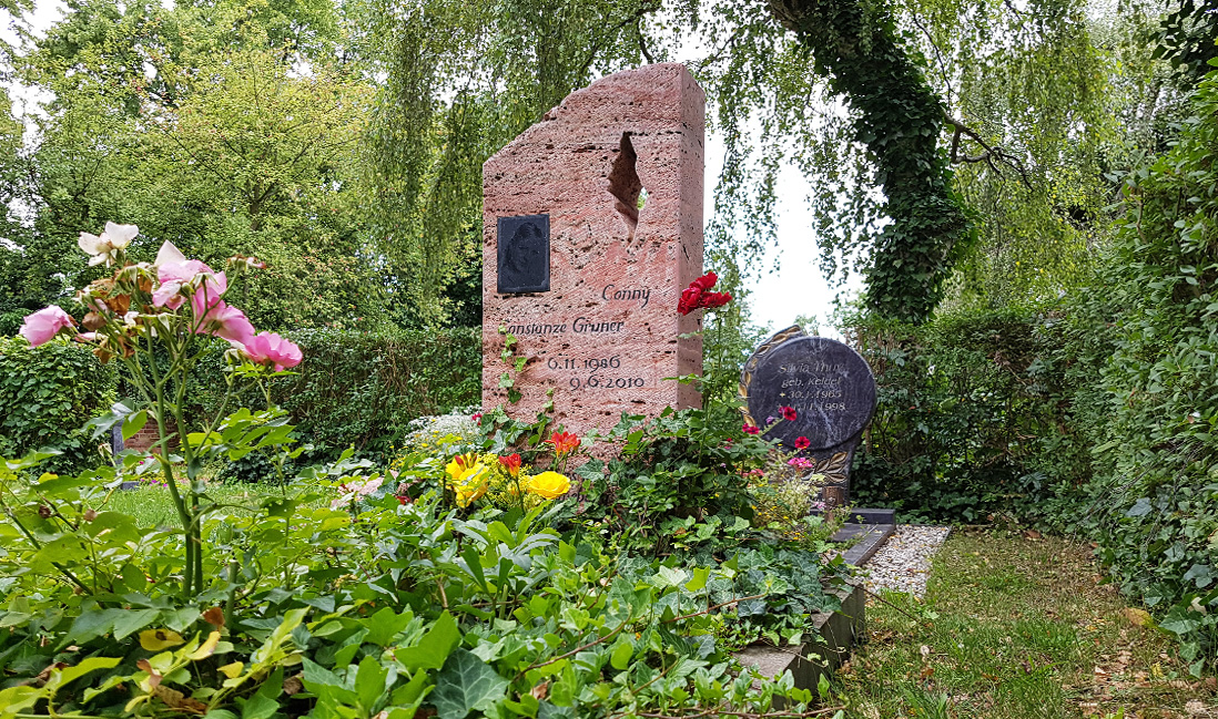 Naturbelassener Grabstein Einzelgrab mit Rosen und Efeu / Grabstein mit Öffnung roter Travertin