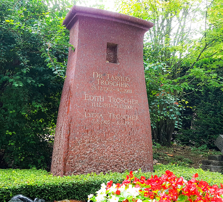 Moderner Doppelgrabstein aus rotem Granit mit kleiner Nische - immergrüne Grabbepflanzung