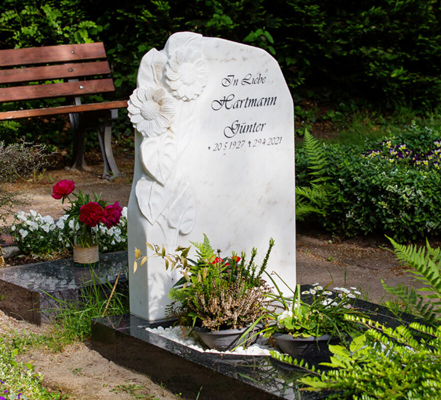 Kleines Urnengrab mit einem Grabstein aus weißem Marmor mit Sonnenblumen und einer Einfassung