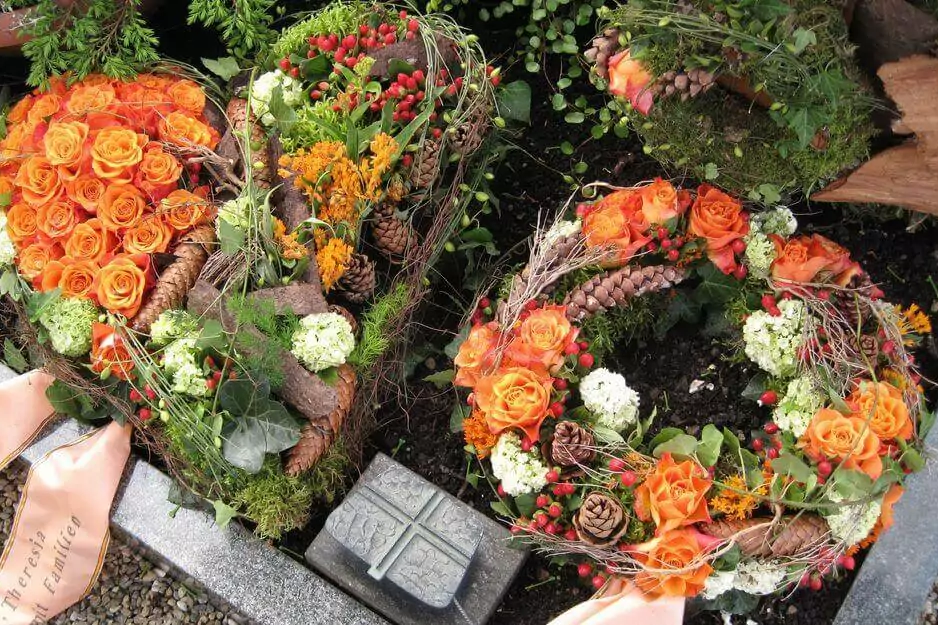 Idee für die Grabgestaltung zum Totensonntag mit verschiedenen Gestecken und Grabkränzen mit orangenen Rosen.