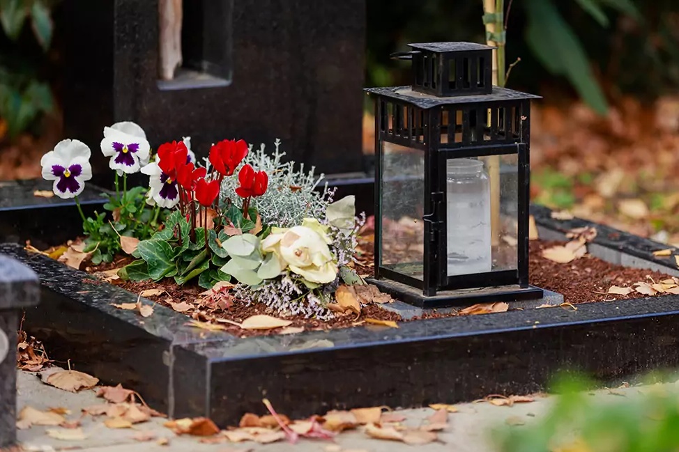 Einfache Grabgestaltung für die kalte Jahreszeit mit Stiefmütterchen und Bodendeckern. Die Grablampe bringt Licht auf das Grab.
