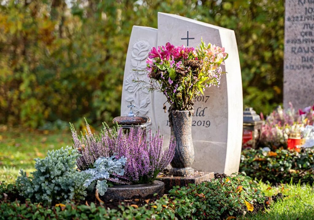 Kleines Urnengrabmal aus hellem Kalkstein mit Rosenmotiv - herbstliche Grabbepflanzung mit Bodendeckern / Nordfriedhof München